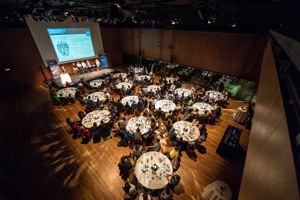 Menschen an runden Tischen und einer Bühne mit Podium im Seestudio im Festspielhaus Bregenz