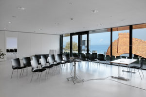 Zwei Stuhlreichen mit schwarzen Stühlen und ein Beamer in der weißen Seegalerie im Festspielhaus Bregenz mit Seeblick