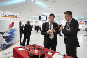 Kongressteilnehmer im Anzug vor einer Ausstellungskoje im hellen Foyer des Festspielhauses Bregenz