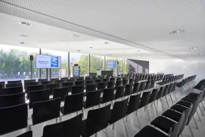 Schwarze Stuhlreihen vor zwei Großbildschirmen im weißen Saal Bodensee im Festspielhaus Bregenz mit Blick auf den Vorplatz © Anja Koehler