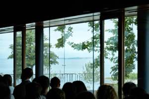 Menschen sitzen in einem Vortrag im Seestudio des Festspielhauses Bregenz mit Blick auf den Bodensee