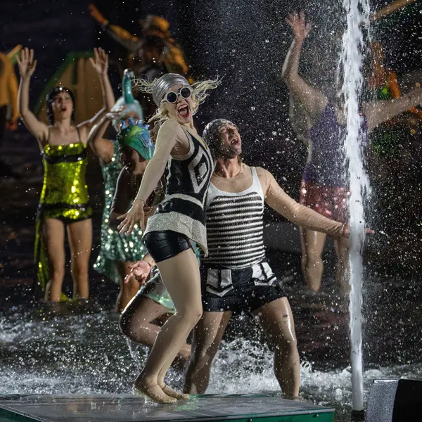 Tänzer:innen und Sänger:innen in bunten Kostümen tanzen im Wasser auf der Seebühne © Bregenzer Festspiele / Daniel Ammann