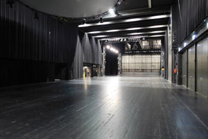 Leere Seitenbühne mit schwarzem Boden, Vorhängen, Rundtraverse und installierter Lichttechnik.